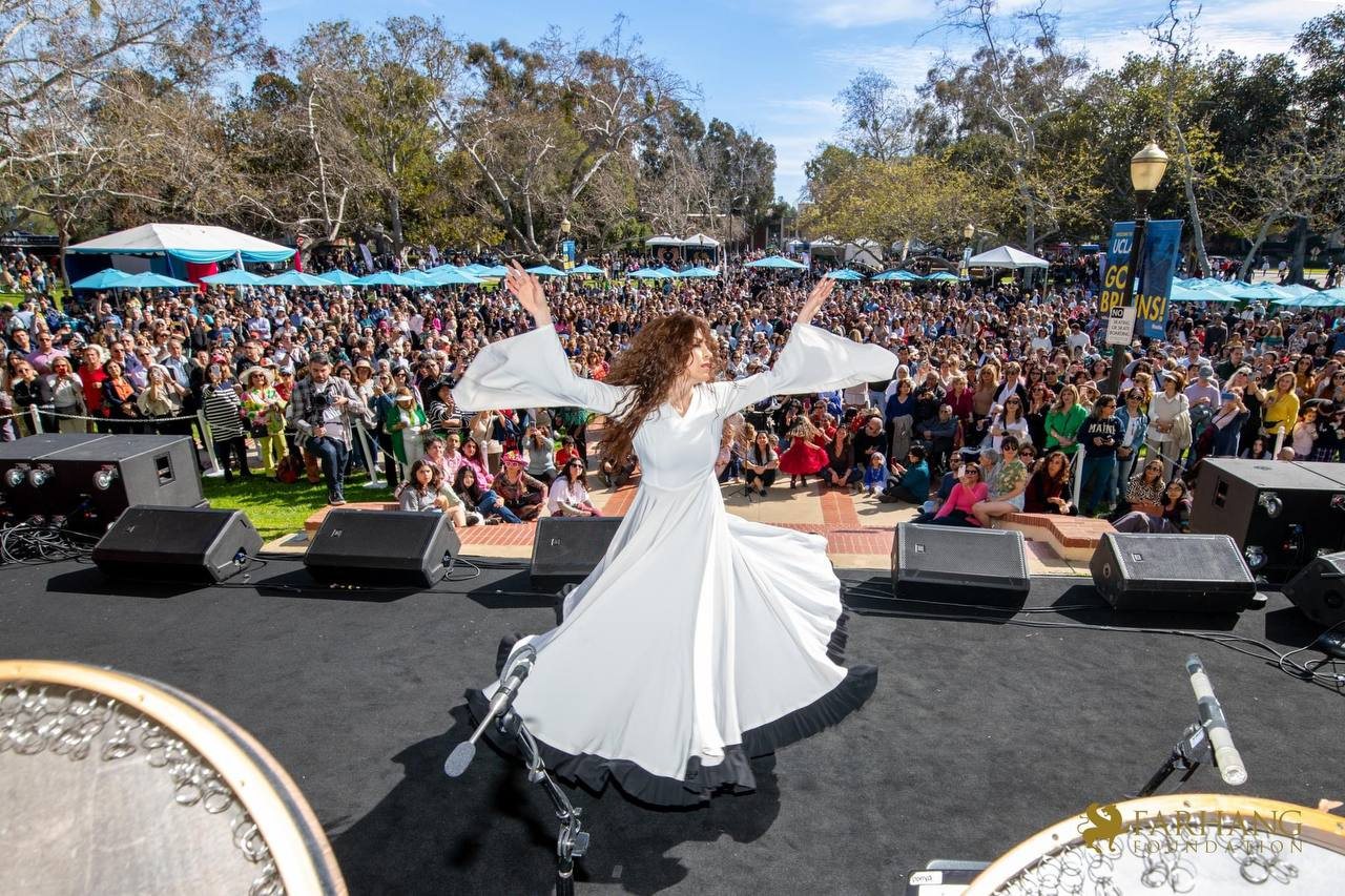 Elham dancing in a flowing white dress on a festival stage in front of a large crowd