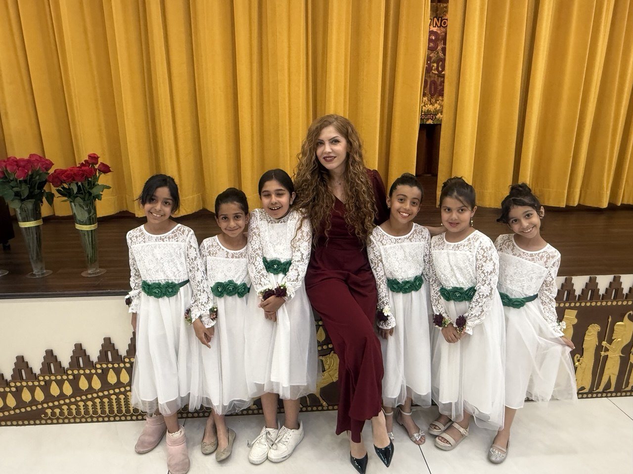 Elham seated with her young dance students in white recital dresses