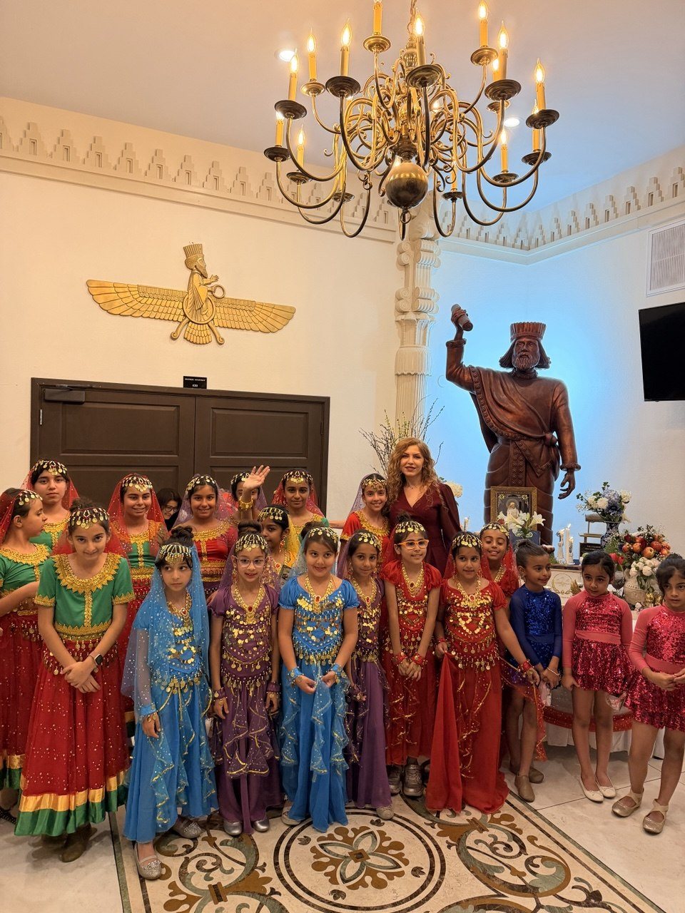 Elham waving with a group of students in colorful dance costumes